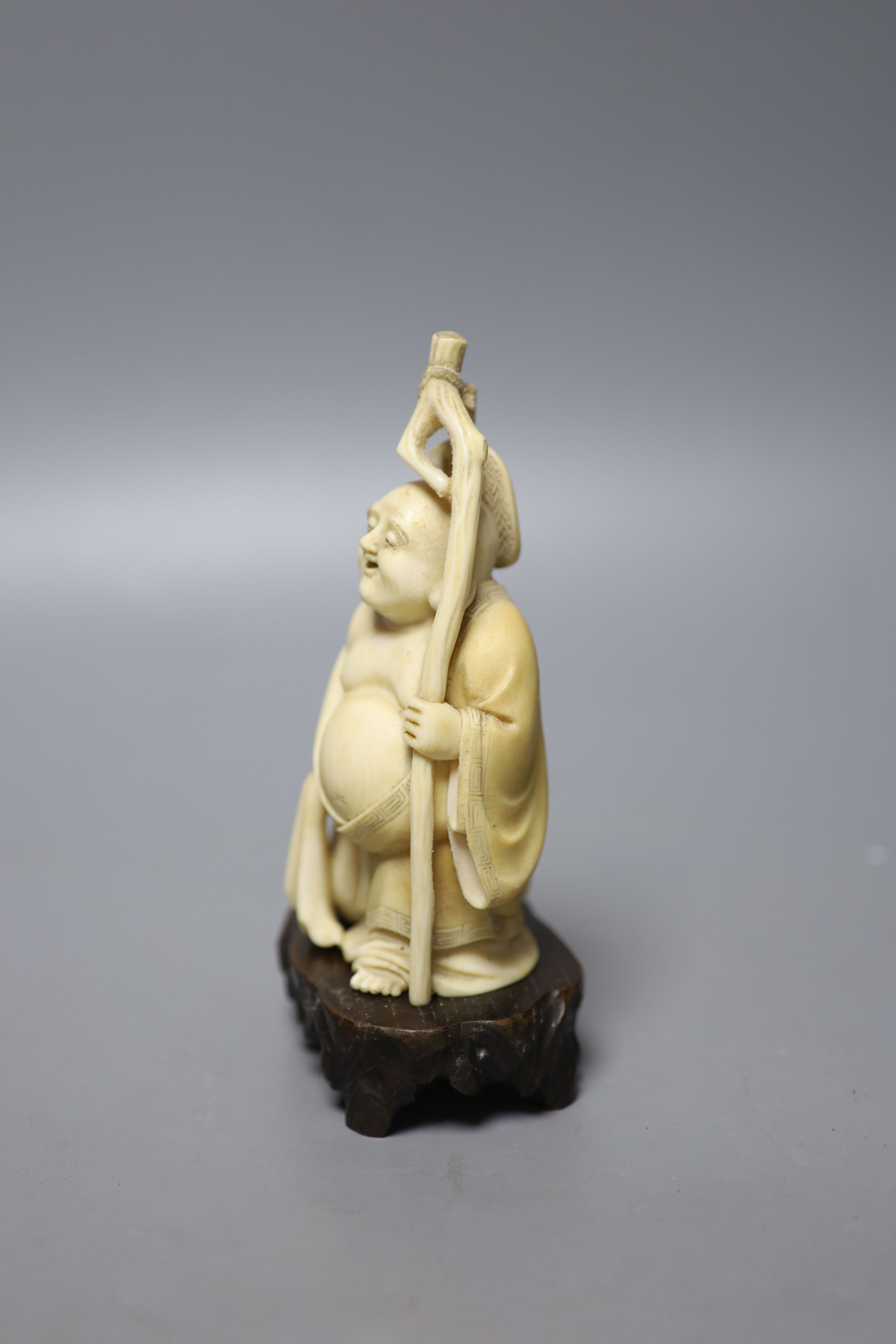 An early 20th century Japanese carved ivory okimono of Hotei, and wood stand, 15cm